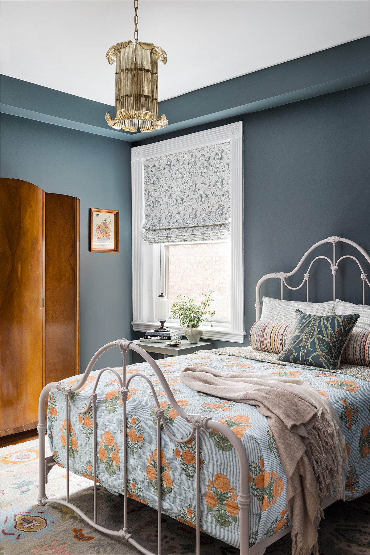 Cozy bedroom with vintage iron bed, floral bedding, blue-gray walls, and a retro gold chandelier