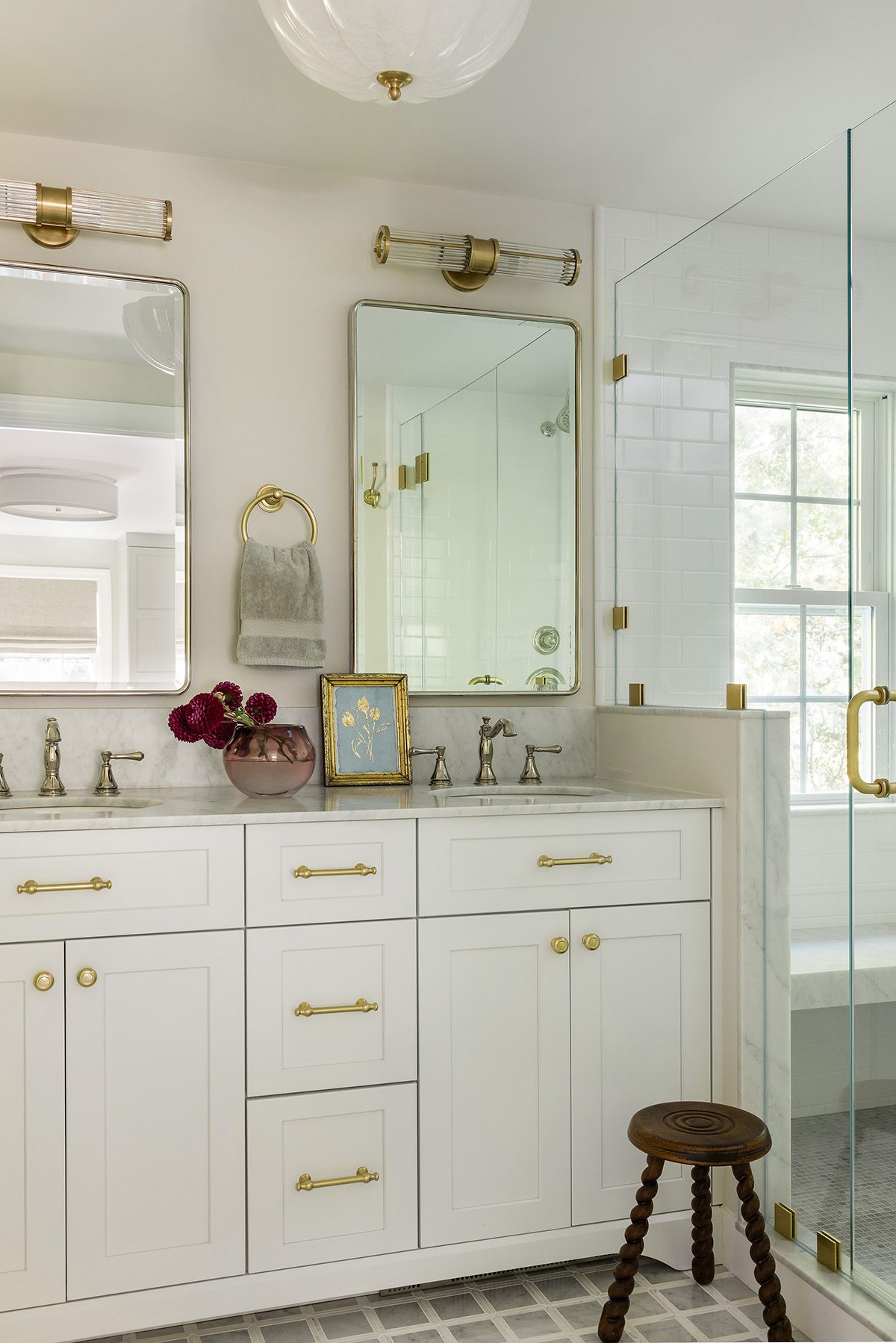 Elegant white bathroom with gold hardware, dual sinks, marble countertops, and glass shower enclosure