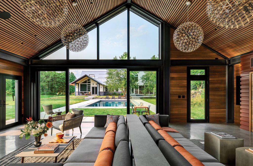 Stylish living space with vaulted ceiling, oversized windows, and a panoramic view of a backyard pool and modern guesthouse.