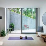 Peaceful home yoga space with sliding glass doors leading to a private outdoor terrace with concrete walls and greenery.