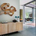 Modern foyer with sculptural wood wall art, a light wood console, and views into a living area with a contemporary fireplace.