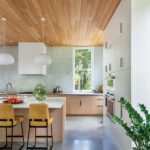 Bright and airy kitchen with natural wood cabinetry, a slatted wood ceiling, island seating, and modern pendant lighting.