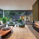 Modern living room with floor-to-ceiling glass, plush seating, and views of a lush courtyard and connected pavilion.