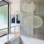 Architectural hallway with hanging mesh pendant lights, vertical slat screen, and framed abstract art.