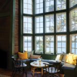 Expansive bay window with built-in bench seating and yellow accent pillows offering panoramic waterfront views.