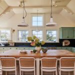 Airy coastal kitchen with light mint green cabinetry, butcher block island, white bar stools, and large pendant lights under a vaulted ceiling.