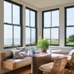 Coastal breakfast nook with panoramic ocean views, built-in bench seating, and a pink resin table in a modern New England home.
