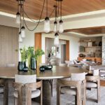 Contemporary dining room with wood ceiling, round wood table, upholstered chairs, and hanging pendant lights in an elegant open-concept space.
