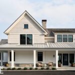 Coastal New England home exterior with shingle siding, large black-framed windows, metal roof, and covered front porch with seating.
