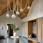 Stylish mudroom with vaulted wood ceiling, custom blue cabinetry, built-in bench, and sculptural pendant lighting in a coastal New England home.