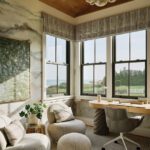 Cozy home office with ocean views, modern desk, textured accent wall, and comfortable lounge seating beneath a bubble chandelier.