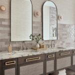 Elegant primary bathroom with dual vanities, marble countertops, arched mirrors, and soft neutral tones in a luxury seaside home.