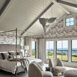 Vaulted-ceiling primary bedroom with canopy bed, ocean views, cozy sitting area, and contemporary cloud-like pendant lights.