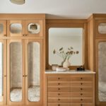 Custom walk-in closet with mirrored cabinet doors, built-in dresser, and large vanity mirror in a refined modern design.