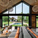 Stylish living space with vaulted ceiling, oversized windows, and a panoramic view of a backyard pool and modern guesthouse.