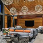 Elegant lounge area featuring a wraparound sectional, orange accent pillows, and a wood-paneled entertainment wall with mounted flat-screen TV.