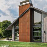 Angular side view of party barn showcasing a rust-toned panel chimney and vertical wood siding against a backdrop of trees and sky.