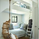 Charming bunk room with a built-in daybed, lofted sleeping area, hanging rattan chair, and coastal-inspired decor.