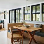 Modern dining nook with a wood banquette, woven chair, and natural light streaming through black-trimmed windows.