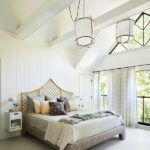 Airy primary bedroom with vaulted ceilings, a rattan headboard, soft neutral bedding, and oversized pendant lights above a serene retreat.
