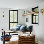 Cozy reading nook with a woven daybed, striped pillows, round rattan coffee table, and natural light streaming through black-trimmed windows.