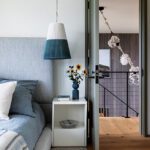 Tranquil bedroom featuring a blue upholstered bed, minimalist nightstand, and pendant light with a view into a modern stairwell