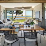 Open-concept dining and living area with wood accents, coastal decor, and sliding glass doors framing panoramic ocean views"