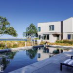 Sleek contemporary home with geometric architecture and a waterfront pool surrounded by natural landscaping
