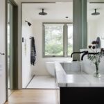 Luxurious bathroom featuring a marble vanity, black fixtures, freestanding tub, and large windows with woodland views
