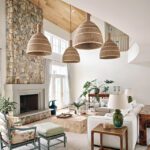 Coastal-inspired living room with a stone fireplace, woven pendant lights, and vaulted wood ceiling in a modern Cape Cod home.
