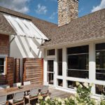 Private outdoor dining space with wooden table and chairs, surrounded by hydrangeas and a white shingle facade.