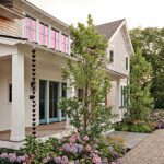 Charming side view of Cape Cod home with blooming hydrangeas, gravel path, and turquoise double doors beneath a covered porch.