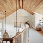 Second-floor landing with vaulted wood ceilings, a curved railing, and cozy window seat with built-in bookshelves.