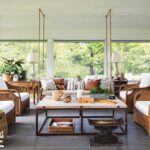 Relaxed screened porch living area with wicker furniture, neutral cushions, hanging swings, and lush garden views.