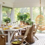 Inviting screened porch dining setup with wicker chairs, whitewashed table, hanging rattan swing, and potted plants.