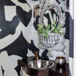 Artistic powder room featuring bold black and white mural walls, a carved stone mirror, and a dark wood vanity with a metallic sink.