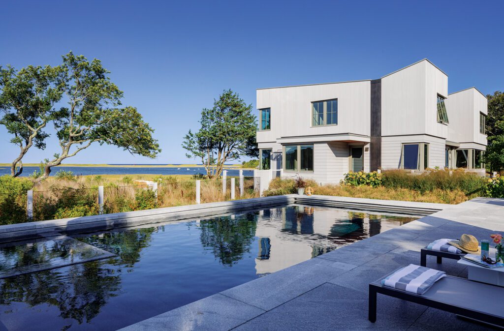 Sleek contemporary home with geometric architecture and a waterfront pool surrounded by natural landscaping