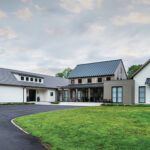 Modern farmhouse with metal roof, wood and stucco facade, and a wide driveway set on a manicured green lawn.