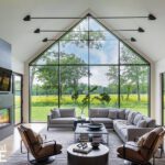 Bright, modern living room with vaulted ceiling, sleek fireplace, and floor-to-ceiling windows revealing a scenic meadow.