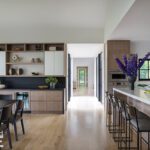 Light-filled modern kitchen featuring a large island, built-in bar cabinetry, and a hallway with black-framed windows.