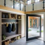 Organized mudroom with built-in cubbies, coat storage, and a large pivoting glass door opening to the courtyard.
