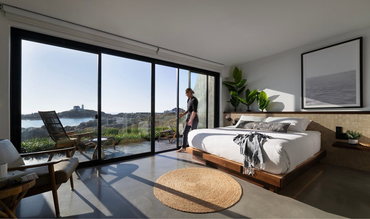 Spacious modern bedroom with Marvin multi-slide glass doors opening to a coastal view, blending indoor and outdoor living.
