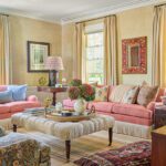 Charming living room with coral pink sofas, floral textiles, a textured ottoman, and layered vintage rugs in a cozy, light-filled setting.