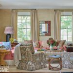 Bright and inviting living room with patterned armchairs, coral seating, botanical pillows, and large windows with cream curtains.