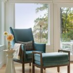 Midcentury-inspired reading nook with a teal lounge chair and ottoman, sculptural side table, and expansive window views.