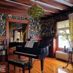 Moody music room with bold botanical wallpaper, dark wood trim, green glass chandelier, and a grand piano.