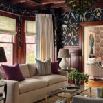 Richly paneled living room with ornate fireplace, graphic wallpaper, and cozy seating arranged around a glass coffee table.