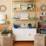 Stylish shelving display with colorful glassware, woven ottomans, and decorative pillows in a coastal-themed interior at Living Swell boutique.
