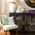 Modern seating area with a white accent chair, textured pillows, and a black cabinet showcasing designer fabric swatches beneath elegant ceramic lamps.