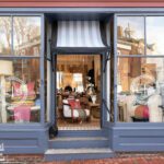Exterior view of Living Swell boutique in Marblehead with blue-painted facade, striped awning, and charming window displays of home decor.
